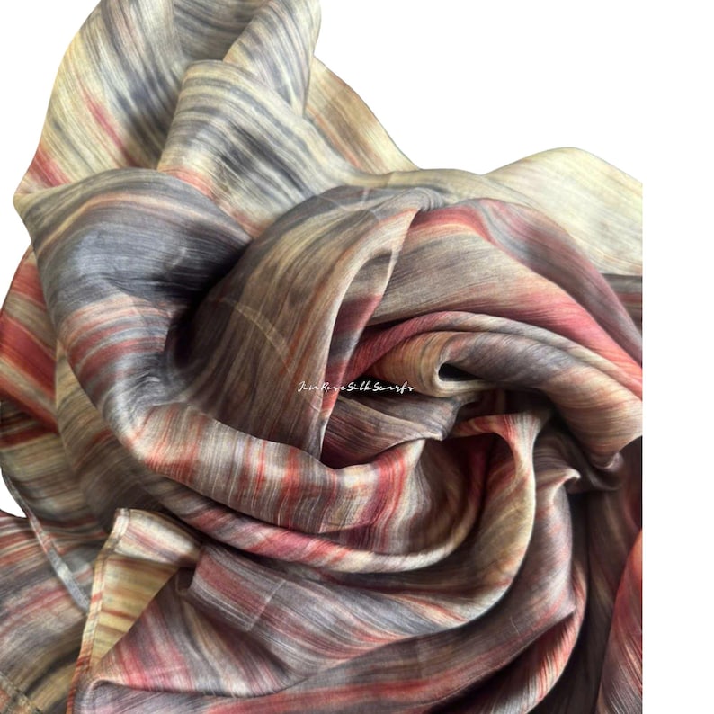 May include: A lightweight scarf featuring a multi-coloured abstract pattern with vertical streaks of deep charcoal, muted red, and soft cream tones. The fabric has a subtle sheen and a delicate, flowing texture with the text Jini Rose Silk Scarfs.