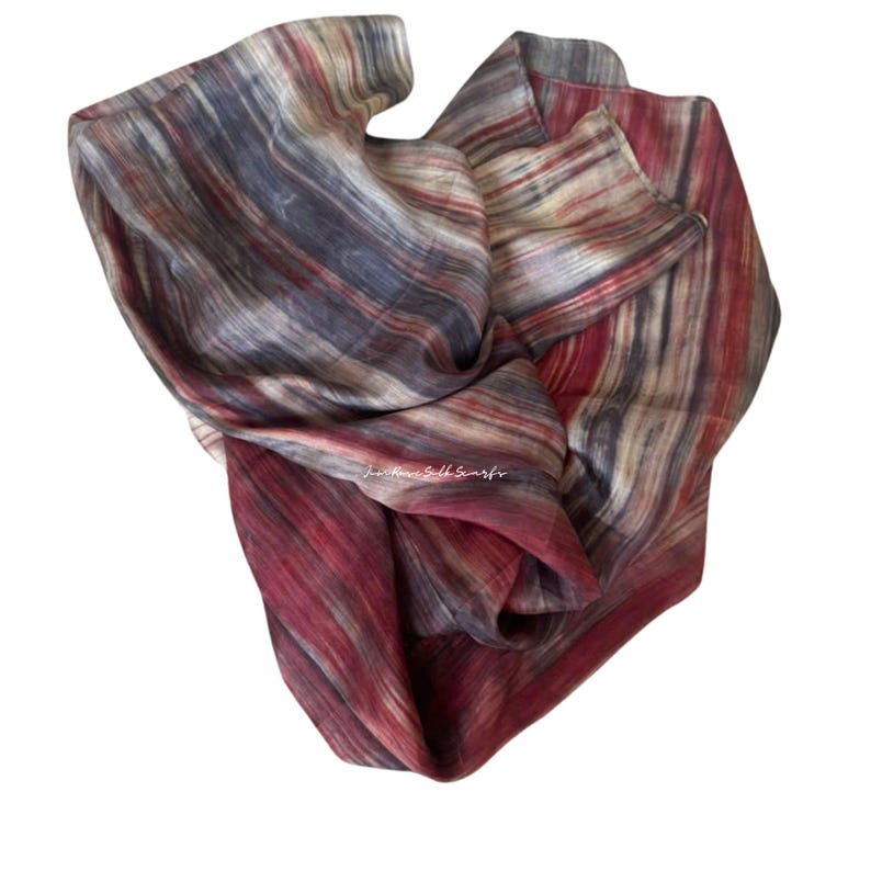 May include: A lightweight scarf featuring a vertical striped pattern in shades of deep red, charcoal grey, and off-white. The fabric has a subtle sheen and a fluid drape. The text "Just Hand Silk Scarfs" is printed in white in the centre.