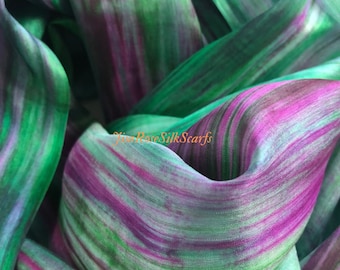 May include: A green and purple silk scarf with a hand-painted abstract design. The scarf is made of soft, flowing silk and is perfect for adding a touch of elegance to any outfit.