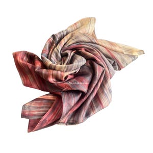 May include: A square silk scarf featuring a multi-coloured abstract pattern with vertical stripes in shades of deep red, muted orange, soft beige, and charcoal grey. The fabric is gathered in the centre, displaying a fluid, draped texture throughout.
