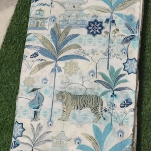 May include: A folded fabric featuring a repeating pattern in shades of blue, green, and white. The design includes illustrations of tigers, palm trees, pagodas, and geometric star shapes, creating a detailed scene across the textile surface.