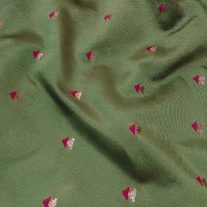 May include: An olive green fabric featuring a repeating pattern of small, embroidered motifs. Each motif consists of a vibrant magenta top section paired with a metallic gold base, creating a consistent, evenly spaced design across the textile surface.