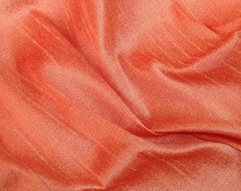 May include: Close-up of a peach-colored fabric with a subtle sheen. The material is gathered and folded, creating soft shadows and highlights. The texture appears smooth with visible vertical lines.