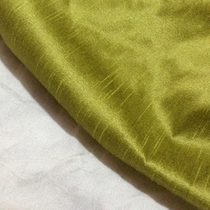 May include: Close-up of a section of green fabric with a textured surface. The fabric has a slight sheen and appears to be folded over a white fabric. The green fabric has subtle vertical lines.