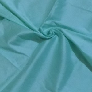 Puede incluir: Una tela suave de color azul claro con una textura suave y fluida. La tela está doblada y drapeada, creando una sensación de movimiento y fluidez.