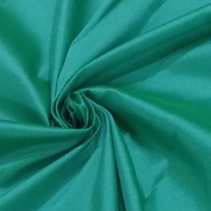 May include: A close-up of a vibrant emerald green fabric with a silky sheen. The fabric is artfully draped and swirled, creating soft folds and shadows. The material appears smooth and luxurious, suitable for apparel or home decor.