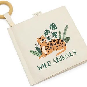 May include: A beige fabric book with a wooden ring attached. The book features a colorful illustration of a leopard with green leaves and the text "WILD ANIMALS".