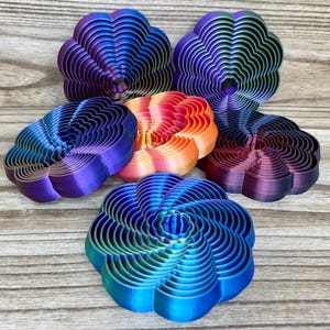 May include: Six circular, flower-shaped objects with concentric, rippled, and layered designs. The objects feature a gradient of colors including blue, purple, green, orange, and pink. Each piece has a distinct, ridged, and textured surface.