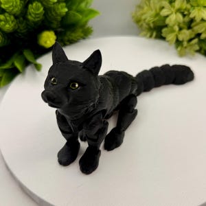 May include: A matte black articulated fox figurine with a segmented body and tail. The fox has pointed ears, a detailed snout, and small, light-colored eyes. The figure is constructed with visible joints that allow for movement and posing.