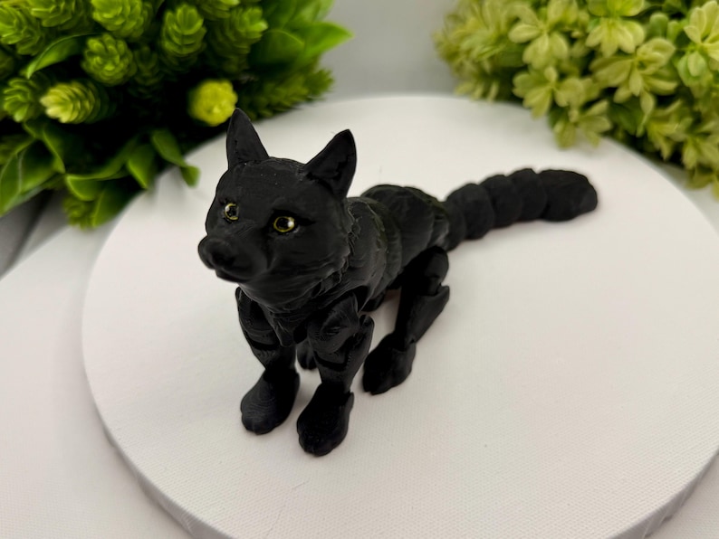 May include: A matte black articulated fox figurine with a segmented body and tail. The fox has pointed ears, a detailed snout, and small, light-colored eyes. The figure is constructed with visible joints that allow for movement and posing.