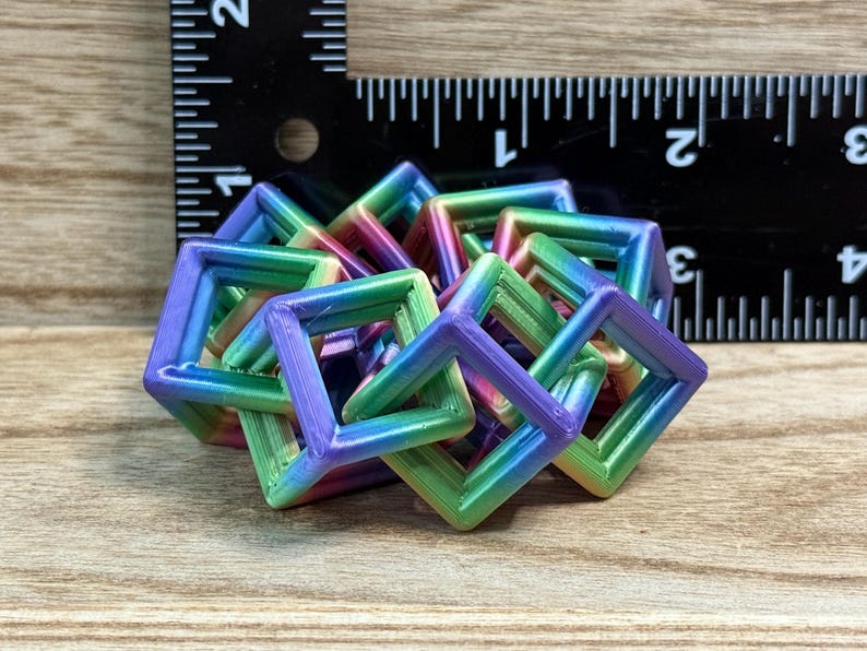 Pode incluir: Uma escultura geom&eacute;trica multicolorida impressa em 3D composta por molduras quadradas interligadas. A escultura exibe um gradiente de cores, incluindo verde, azul, roxo e rosa. Uma r&eacute;gua no fundo mostra medidas em cent&iacute;metros.