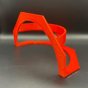 May include: A bright orange plastic protractor with a hexagonal base and a curved ruler. The protractor is marked with numbers from 0 to 180 degrees. The protractor is designed for measuring angles and is a useful tool for students, artists, and craftspeople.