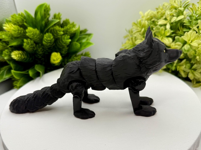 May include: A matte black articulated fox figurine featuring a segmented body design that allows for movement. The fox has pointed ears, a textured coat, and a long tail, standing on four legs with visible joints at the shoulders and hips.