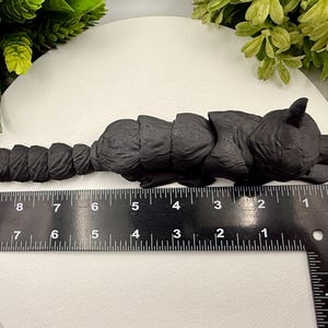 May include: A matte black articulated fox figurine with a segmented body and tail, positioned alongside a black ruler. The ruler indicates the fox measures approximately 9 inches in total length from the tip of the nose to the end of the tail.