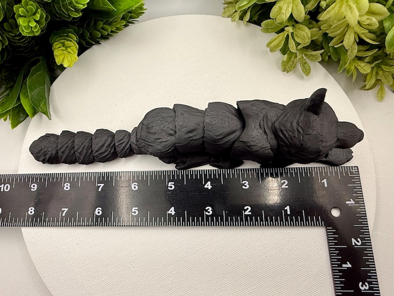 May include: A matte black articulated fox figurine with a segmented body and tail, positioned alongside a black ruler. The ruler indicates the fox measures approximately 9 inches in total length from the tip of the nose to the end of the tail.
