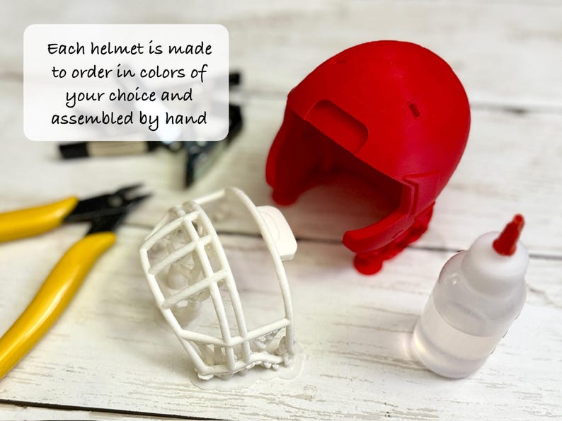 Puede incluir: Una carcasa de casco de color rojo brillante y una m&aacute;scara facial blanca, acompa&ntilde;adas de unos alicates con mangos amarillos y un peque&ntilde;o frasco de adhesivo transparente. El texto dice: Each helmet is made to order in colors of your choice and assembled by hand.