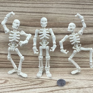 Puede incluir: Tres figuras de esqueleto de plástico blanco en diferentes poses sobre un fondo de madera. Los esqueletos están articulados en las articulaciones y tienen una estructura ósea realista.