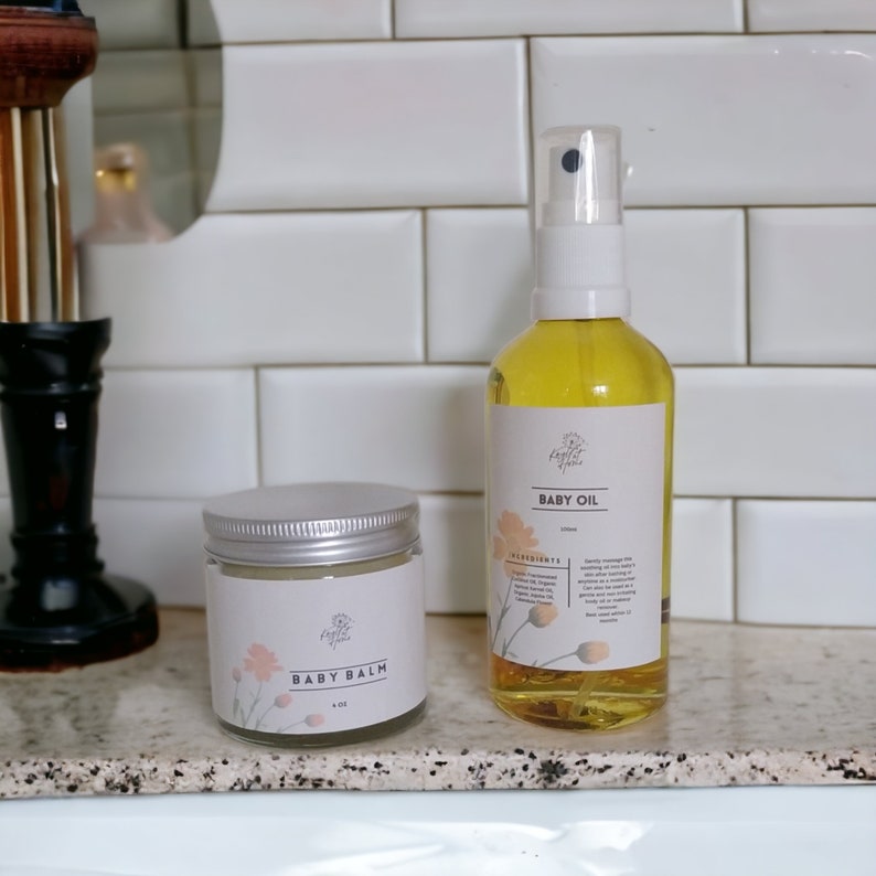May include: A set of baby care products, a white jar labeled "Baby Balm" with a floral design and a clear glass bottle labeled "Baby Oil" with a floral design. Both products are on a white tiled surface.