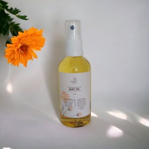 May include: A clear glass bottle with a white spray top filled with yellow baby oil. The bottle has a white label with the text "BABY OIL" and a list of ingredients.
