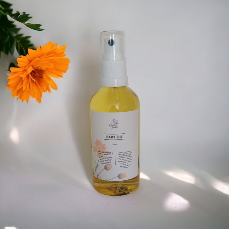 May include: A clear glass bottle with a white spray top filled with yellow baby oil. The bottle has a white label with the text "BABY OIL" and a list of ingredients.