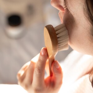 Facial dry brushing with Kayle at Home brush, gently gliding over the skin to encourage blood flow and enhance skincare absorption.