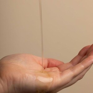 May include: A hand with a clear liquid dripping onto it from above.