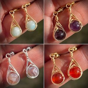 May include: Four pairs of gold-toned wire wrapped earrings with different coloured gemstone drops. The earrings feature a teardrop shape with a wire cage design. The gemstones are amethyst, carnelian, agate, and aventurine.