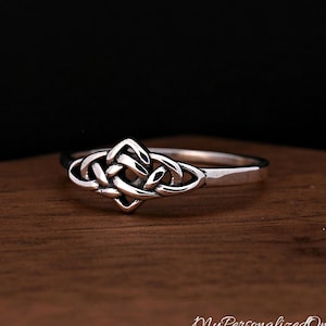 May include: A silver ring featuring a central Celtic knot design with intricate, polished metal loops. The band is smooth and tapers towards the back, showcasing a reflective finish that highlights the detailed, interwoven pattern of the knotwork.