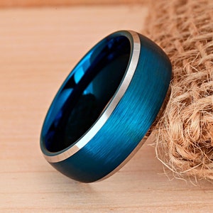 May include: A blue and silver tungsten carbide ring with a brushed finish. The ring is a classic style and has a beveled edge.