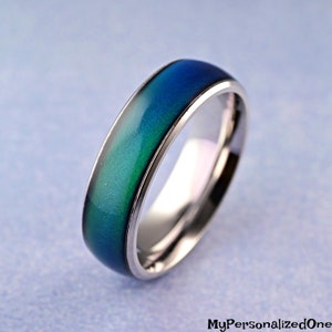 May include: A silver mood ring with a blue and green color-changing stone. The ring is a simple band style.