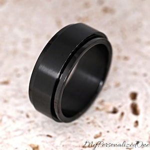 May include: A solid black ring with a smooth, matte finish and a central spinning band feature. The ring has a wide, flat profile with beveled edges. The text MyPersonalizedOne is visible in the bottom right corner of the image frame.
