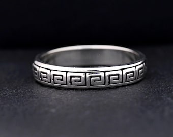 Peut inclure: Une bague en argent avec un motif de clé grecque autour du bandeau. La bague est en métal brillant et présente un design simple et élégant. La bague est présentée sur un fond sombre. Le texte "MyPersonalizedOne" est en bas à droite.