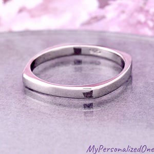 May include: A polished silver-toned ring with a smooth, rounded square band. The interior of the band features a small, stamped hallmark indicating the metal purity. The ring has a reflective, metallic finish and a simple, clean, continuous design.