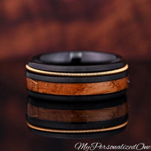 May include: A black ring with a wood grain center band and a gold-colored wire inlay. The ring has a polished finish and a reflective surface. The text "My Personalized One" is at the bottom.