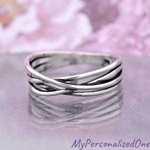 May include: A polished silver ring featuring a multi-strand crossover design. The band consists of several thin, smooth, and interconnected silver wires that overlap to create a layered appearance with dark recessed areas between the metal strands.