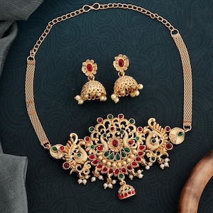 May include: A gold necklace with a peacock design and red and green gemstones. The necklace comes with a pair of matching earrings with red gemstones.