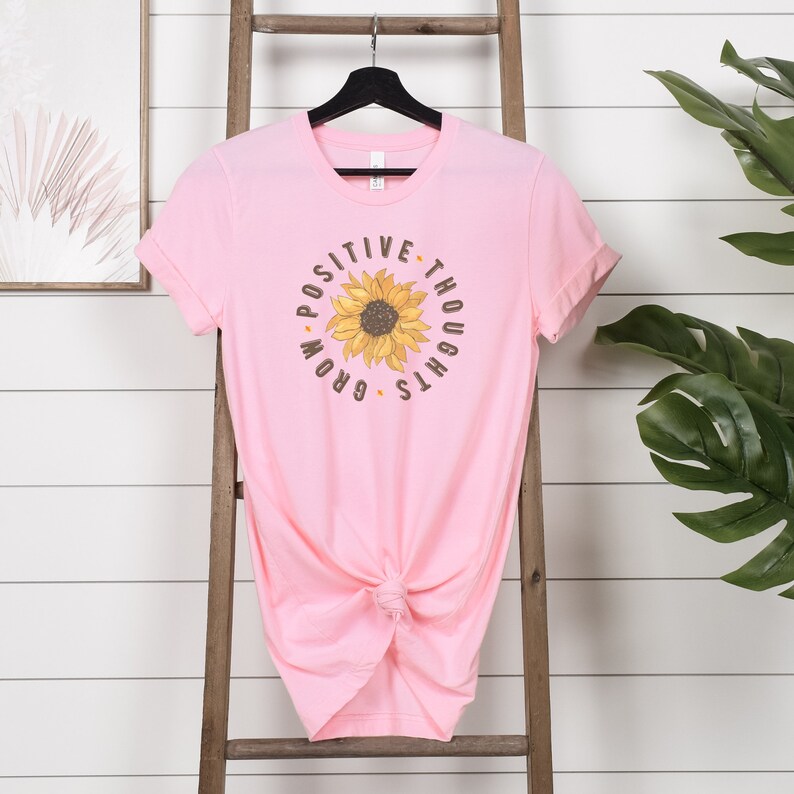 May include: Pink t-shirt with a sunflower graphic and the text "Positive Thoughts Grow".