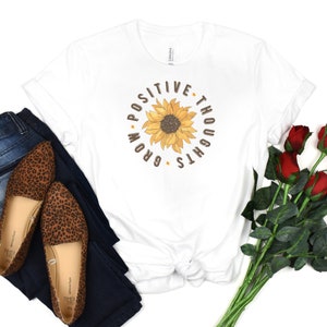 May include: White t-shirt with a sunflower graphic and the text "Positive Thoughts Grow".