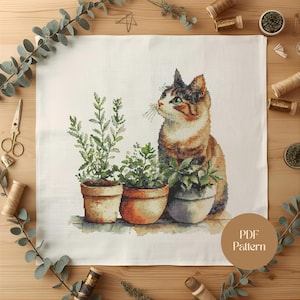 Peut inclure: Motif de point de croix représentant un chat tigré aux yeux verts, à côté de trois plantes en pot. Le chat est brun, orange et blanc. Les plantes sont vertes. Le texte "PDF Pattern" est dans un cercle marron.