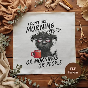 Puede incluir: Un patrón de punto de cruz sobre tela blanca presenta un perro negro con ojos cansados sosteniendo una taza roja. El texto dice: "I DON'T LIKE MORNING PEOPLE OR MORNINGS OR PEOPLE". Hay un patrón PDF disponible.