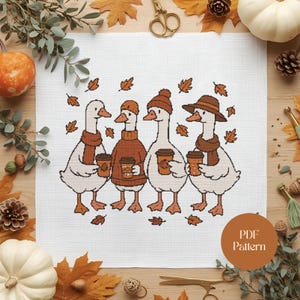 Op de afbeelding: Kruissteekpatroon met vier ganzen in herfstkleding, elk met een koffiekopje. De ganzen dragen sjaals, hoeden en truien, omringd door vallende bladeren. Het ontwerp staat op een wit canvas met een PDF-patroonlabel.