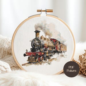 Puede incluir: Bordado de punto de cruz de un tren de vapor vintage, enmarcado en un aro de madera. El tren está detallado con tonos marrones, rojos y negros, con humo visible. El texto "PDF Pattern" está en un círculo en la parte inferior derecha.