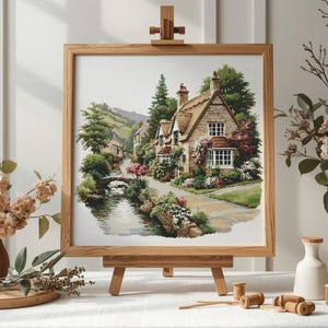 May include: A framed watercolor painting of a quaint village scene, featuring stone cottages with thatched roofs, lush greenery, and a flowing stream. The artwork is displayed on a wooden easel, with floral arrangements in the foreground.
