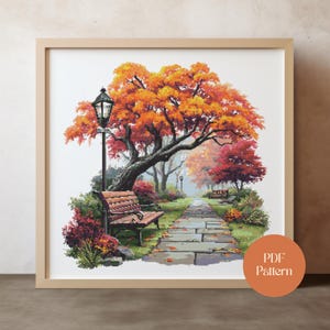 May include: A framed cross-stitch pattern of a park scene in autumn. The image features a stone path, park benches, and trees with vibrant orange and red leaves. A lamppost stands near a bench. The text "PDF Pattern" is in a circle in the lower right.