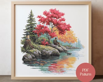 May include: Cross-stitch pattern of a serene lakeside scene. A person is fishing near the water's edge, surrounded by trees with red, yellow, and green foliage. A wooden framed artwork with the text "PDF Pattern" is in the lower right corner.