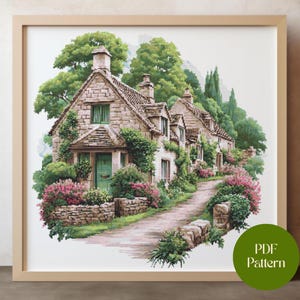 May include: A framed watercolor print of a quaint village scene. Stone cottages with green doors and windows are surrounded by lush greenery and pink flowers. A cobblestone path leads through the village. The print is in a light wood frame.