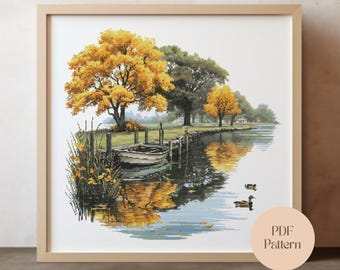 May include: A framed cross-stitch landscape depicts a serene lake scene. A small boat is docked near a wooden pier, with vibrant yellow and green trees reflected in the water. Two ducks swim in the water. The image is labeled "PDF Pattern".