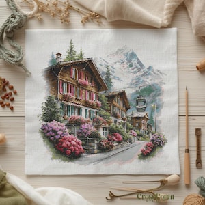 May include: A cross-stitch design depicting a charming European village in a valley, with snow-covered mountains in the background. The buildings feature brown wooden facades, red shutters, and flower boxes. A cable car and vibrant pink and purple flowers are also visible.