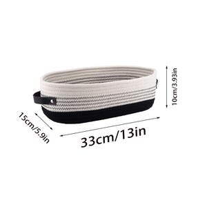 Op de afbeelding: Een wit-zwarte gestreepte opbergmand van katoenen touw met zwarte leren handvatten. De mand is 33 cm lang, 15 cm breed en 10 cm hoog.