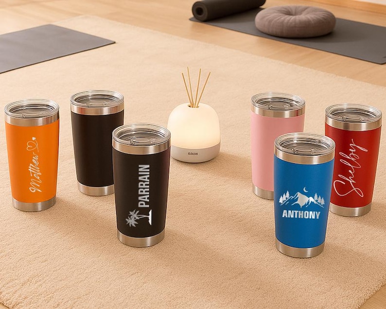 May include: A collection of insulated tumblers in various colors, including orange, black, pink, blue, and red. Each tumbler features a silver lid and personalized text or graphics. The tumblers are displayed on a neutral-toned rug.
